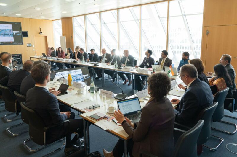 Personen sitzen gemeinsam an einem Tisch und schauen auf einen Bildschirm.