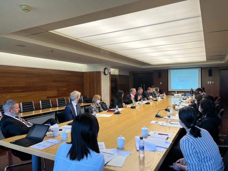 Menschen sitzen an einem langen Tisch vor einer projizierten Präsentation.
