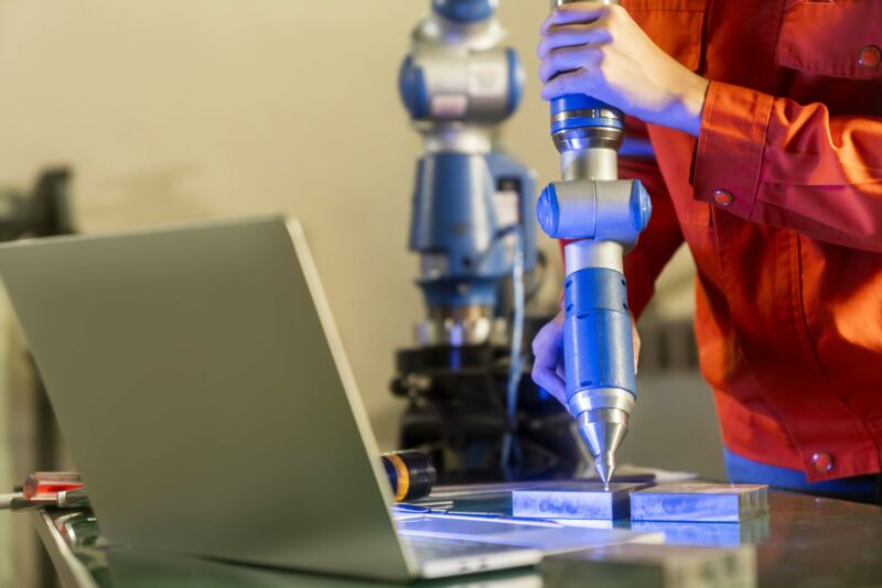 Ingenieurin führt an einer Messmaschine mit Manipulatorarm eine dreidimensionale Koordinatenmessung durch